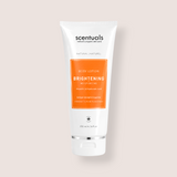 A 200 ml white squeeze tube of Scentuals Brightening Moisturizing Body Lotion, featuring a prominent orange label on the front, set against a solid pale beige background.