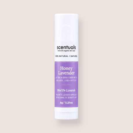A single tube of Scentuals Honey Lavender lip balm centered on a solid, warm off-white background. The tube is white with a lavender purple label and black text.