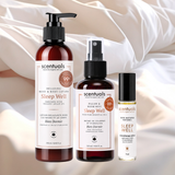 Three Scentuals Sleep Well essential oil and body care products arranged on a soft white satin fabric background: a large pump bottle of relaxing hand and body lotion, a spray bottle of pillow and room mist, and a small vial of 100% natural essential oil.