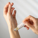 Hand applying a small bottle of cream to another hand against a neutral background